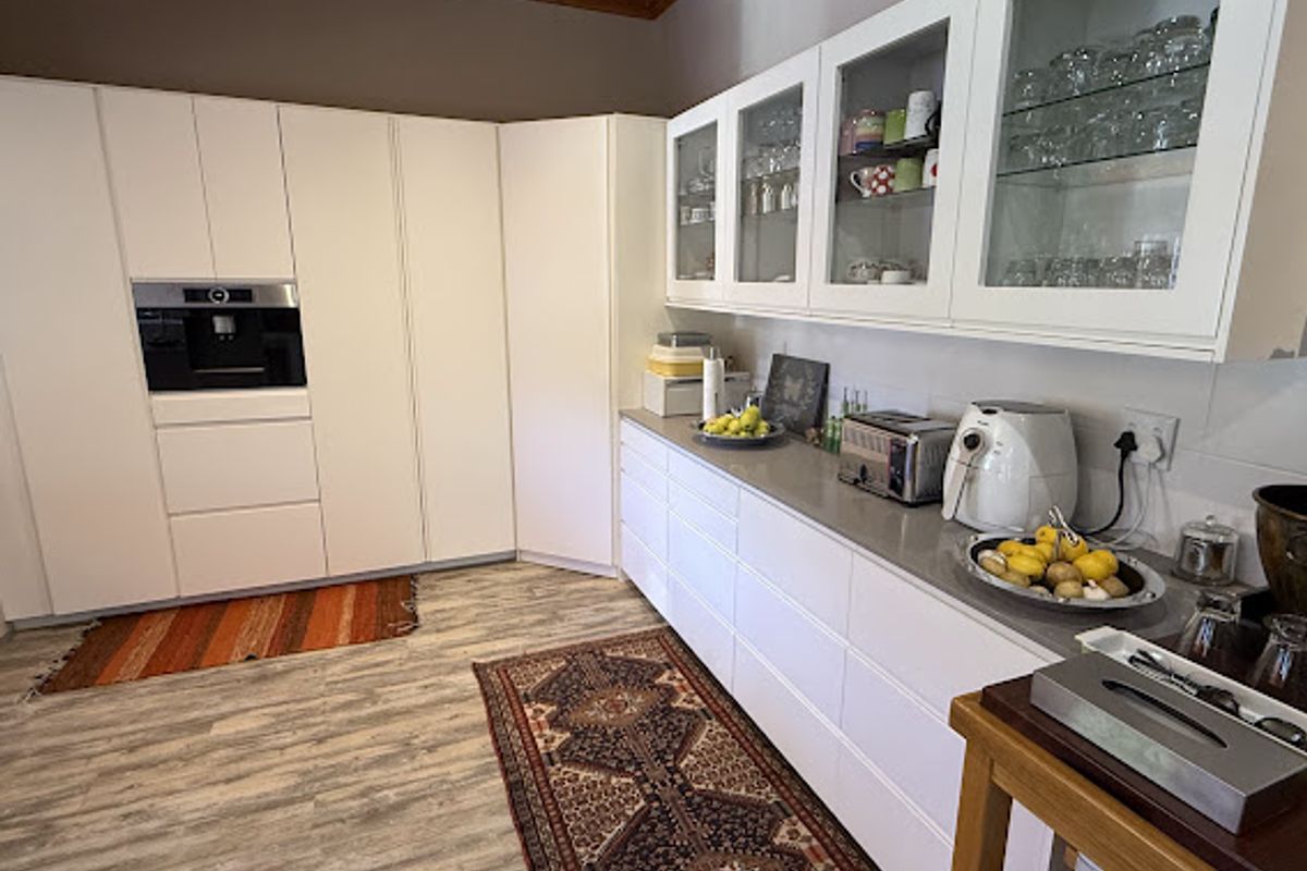 Modern kitchen featuring white handleless cabinetry, stone countertops, glass-fronted display cupboards, integrated coffee machine, and a warm timber ceiling.