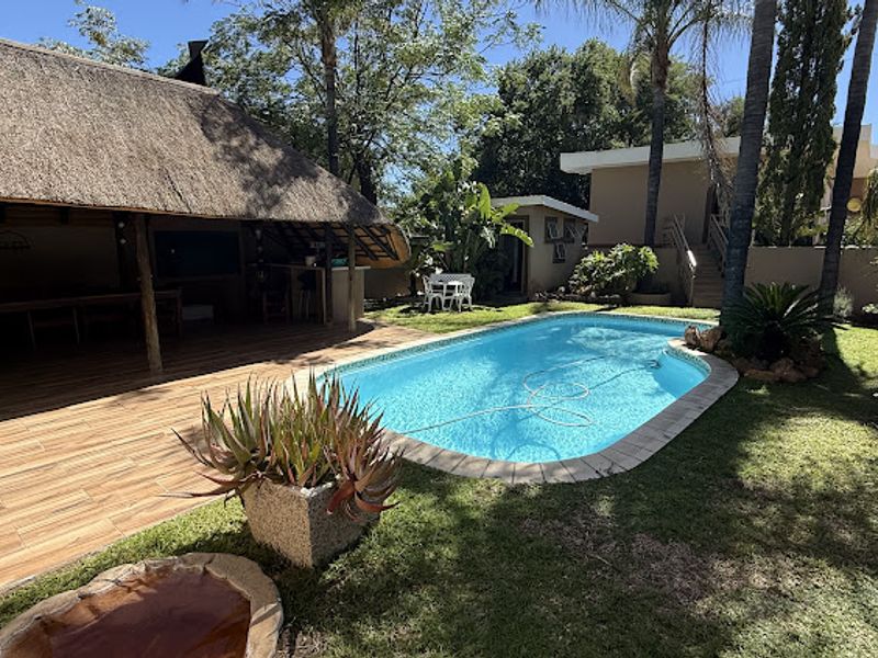 A well-maintained outdoor entertainment area featuring a swimming pool, a spacious thatched lapa, and a landscaped garden setting.