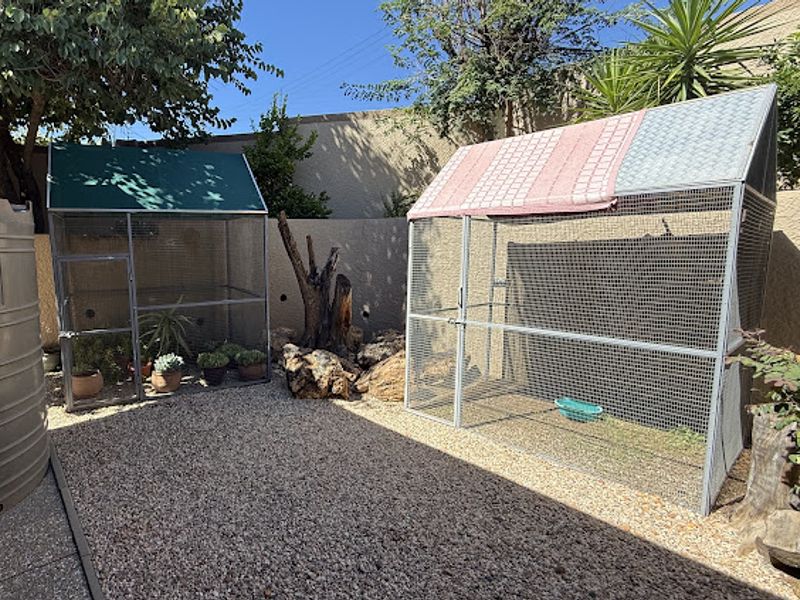 A rear garden area featuring gravel landscaping, a boundary wall, and large metal outdoor enclosures.