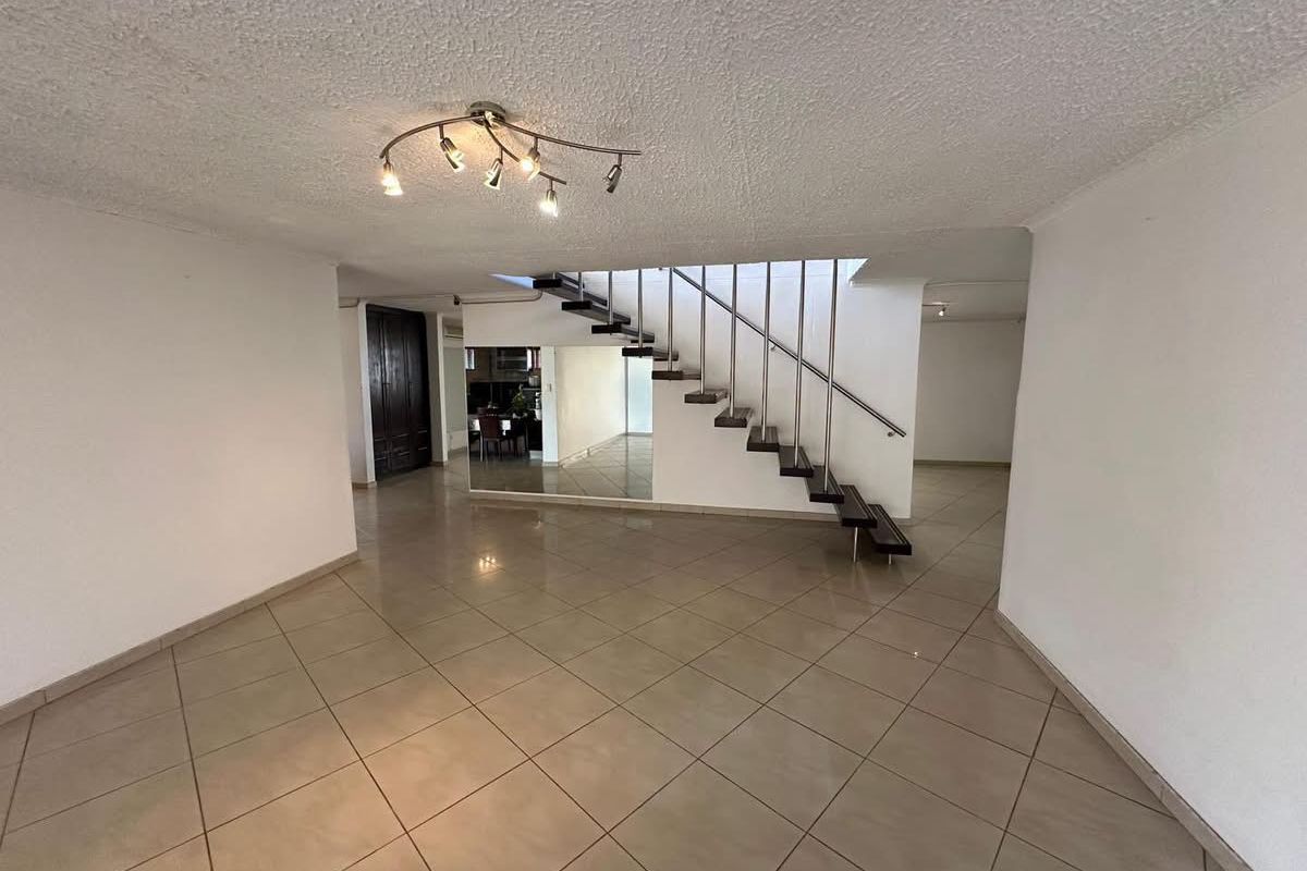 Spacious open-plan living area featuring large format floor tiles, a modern floating staircase with metal railings, and a decorative mirrored wall.