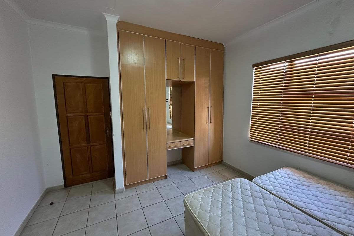 A bedroom featuring built-in wooden cupboards with a vanity section, tiled flooring, and window blinds.