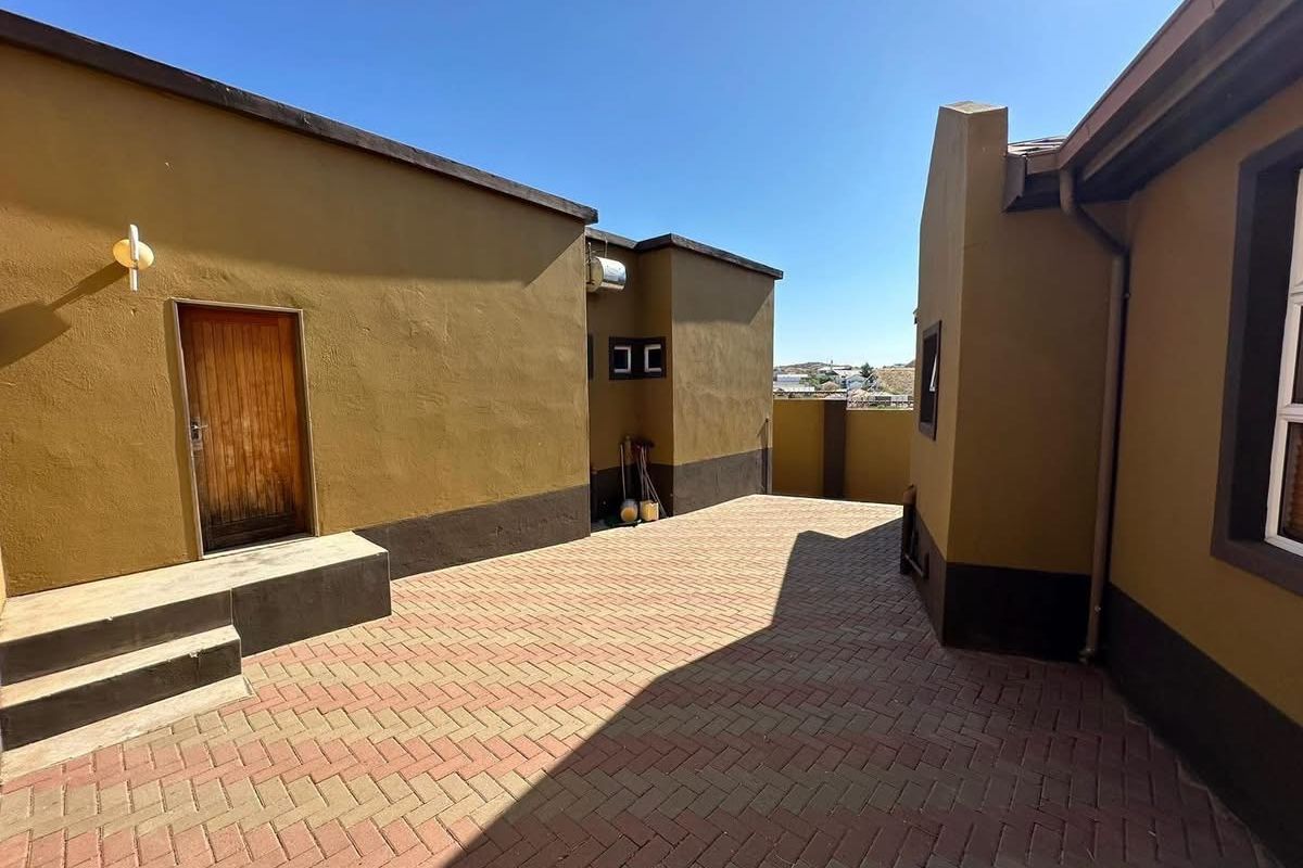 A paved rear courtyard area between building structures, featuring exterior wall lighting and access to a timber door.