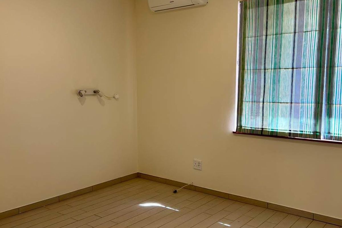 A clean, empty bedroom featuring neutral tiled flooring, a wall-mounted air conditioning unit, and modern track lighting.