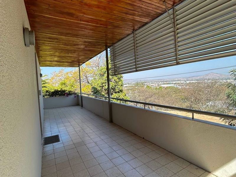 A spacious covered balcony featuring a warm timber ceiling, tiled flooring, and adjustable metal louvre shutters, offering expansive elevated views.