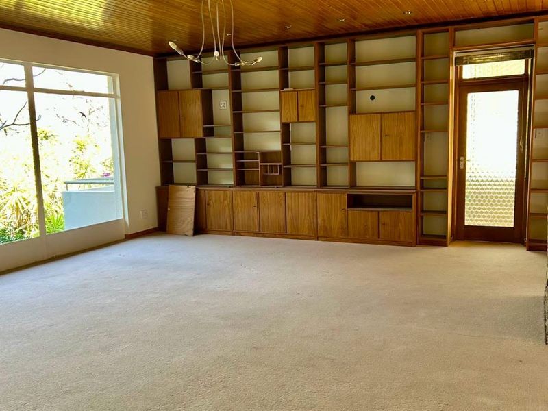 Spacious living room featuring a timber-clad ceiling, extensive built-in wooden shelving, and large windows providing natural light and access to the exterior.