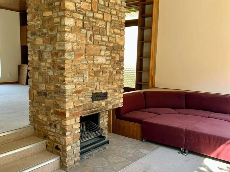 Spacious living area featuring a prominent stone fireplace, timber-clad ceiling, and built-in shelving, offering a cozy and character-filled space.