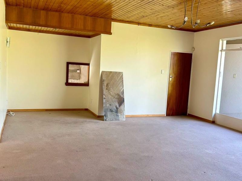 An empty living room featuring a timber tongue and groove ceiling, carpeted flooring, and a standard timber door.