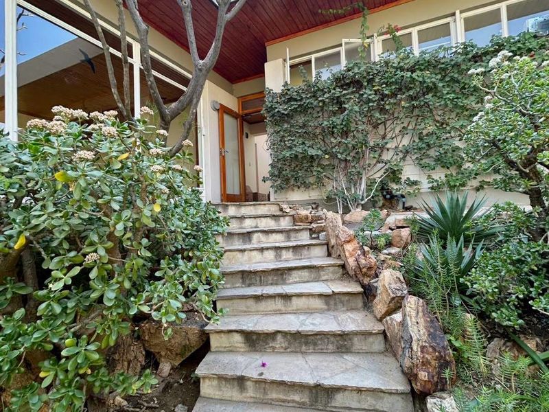A stone staircase leads to the entrance of this home, featuring timber-lined eaves and established rockery gardens surrounding the building facade.