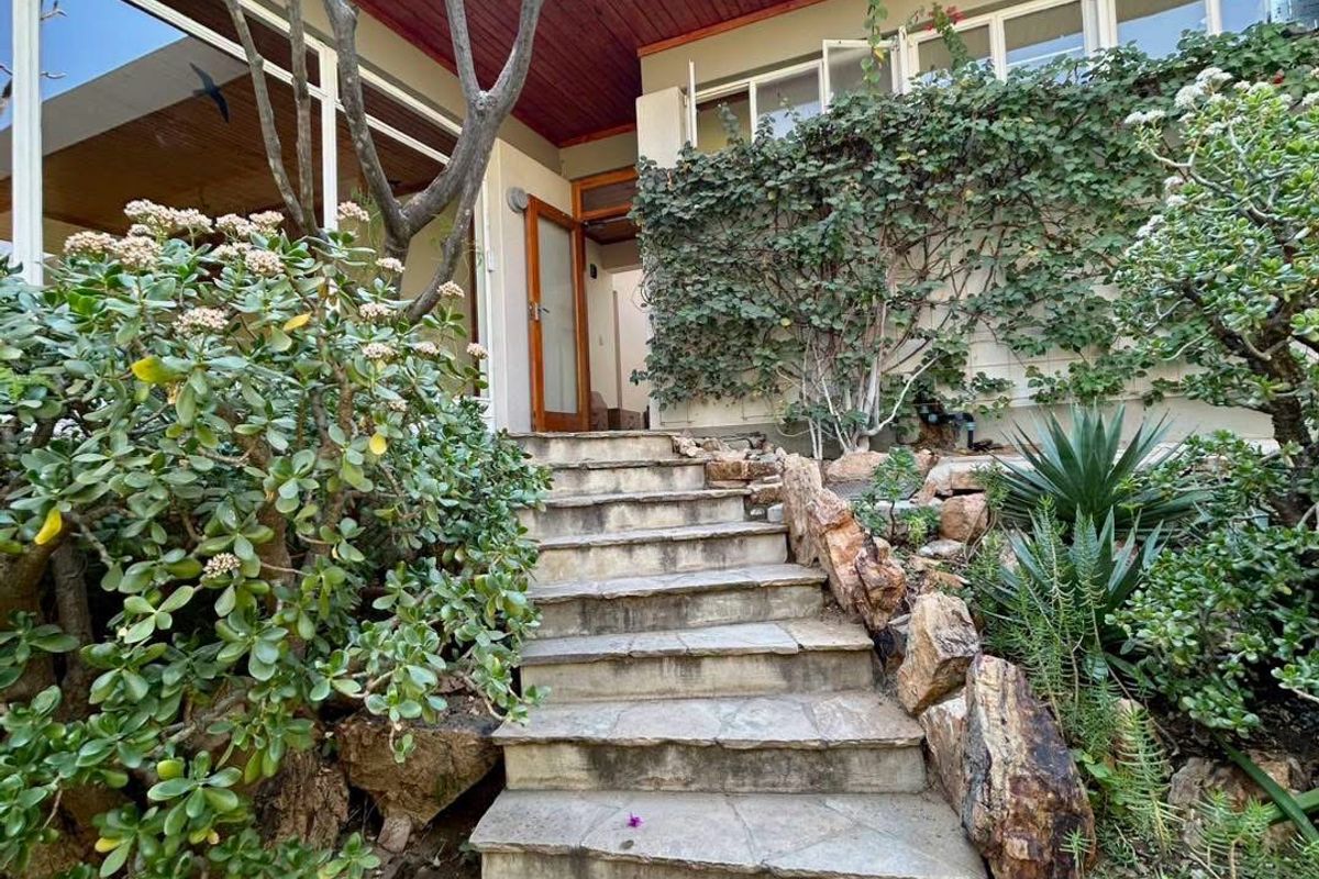 A stone staircase leads to the entrance of this home, featuring timber-lined eaves and established rockery gardens surrounding the building facade.