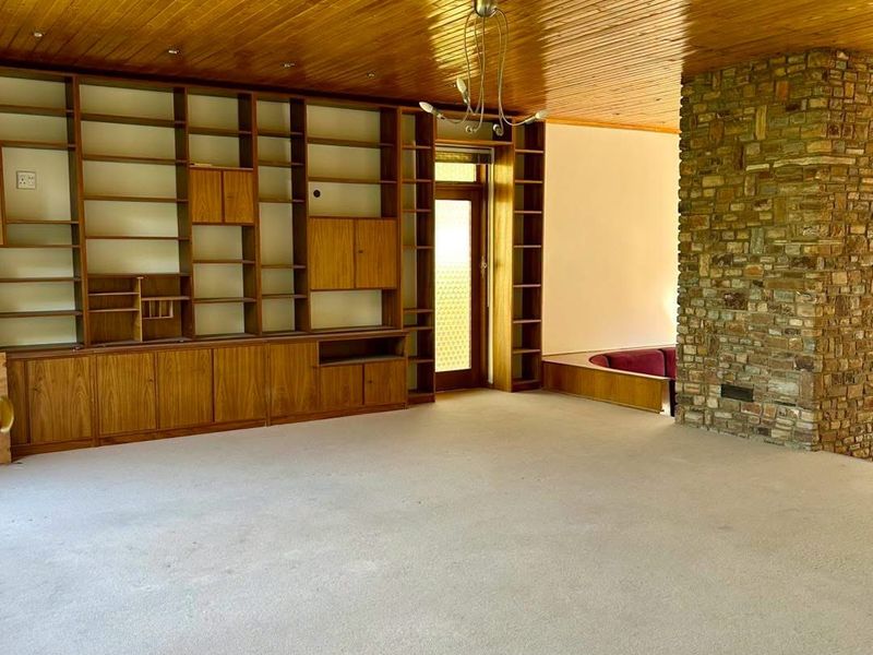 Spacious living room featuring a prominent stone fireplace, extensive built-in wooden cabinetry, and a classic timber-paneled ceiling.