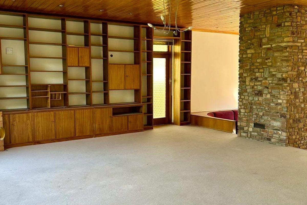 Spacious living room featuring a prominent stone fireplace, extensive built-in wooden cabinetry, and a classic timber-paneled ceiling.