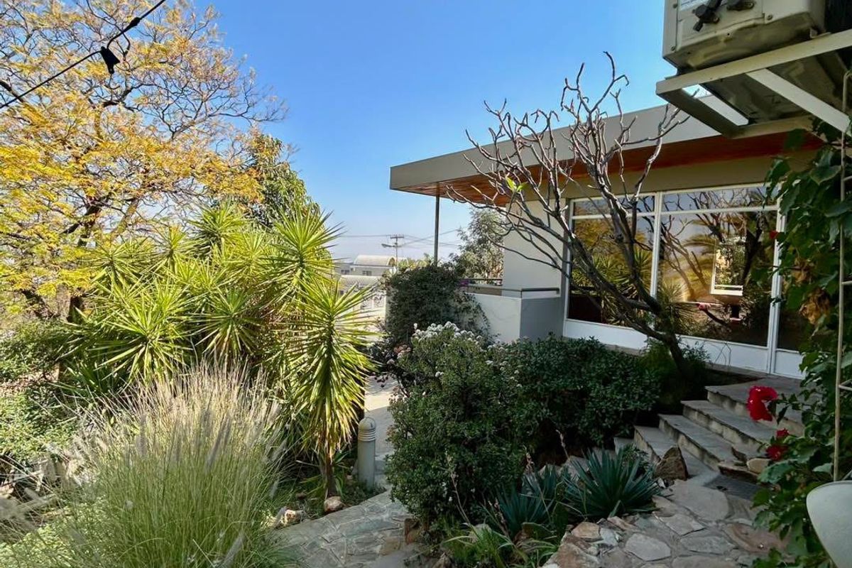 A landscaped rear garden area featuring stone-paved stairs leading to a patio with sliding glass doors and an exterior air conditioning unit.