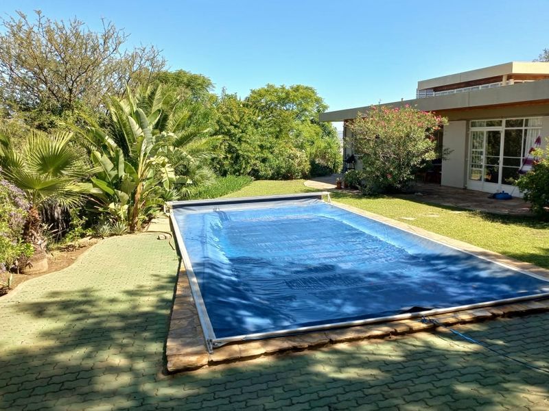 Outdoor pool area featuring a swimming pool with a cover, surrounded by a paved patio and established garden landscaping.