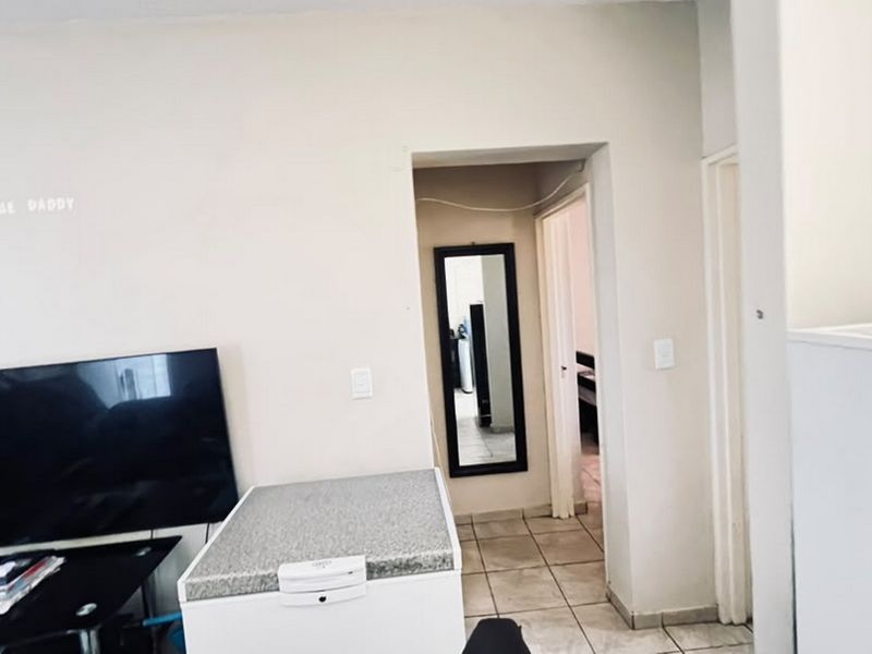 A living area featuring tiled flooring and a doorway leading to an adjacent room, providing a functional layout for the apartment.
