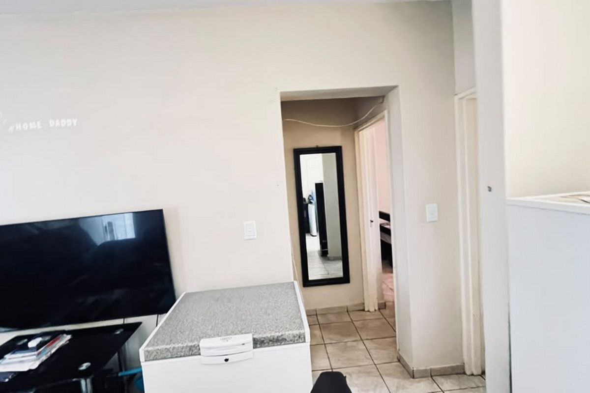 A living area featuring tiled flooring and a doorway leading to an adjacent room, providing a functional layout for the apartment.