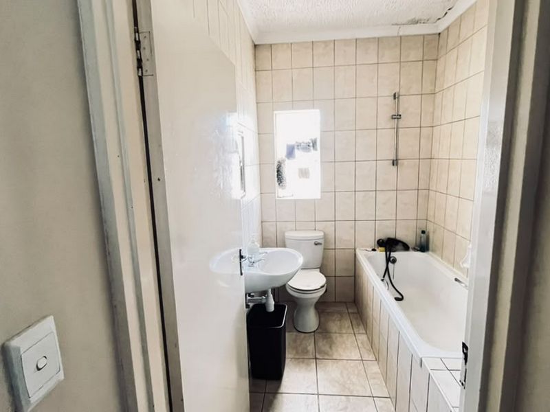 A compact bathroom featuring a bathtub, pedestal basin, and toilet with neutral wall and floor tiling, requiring some ceiling maintenance.