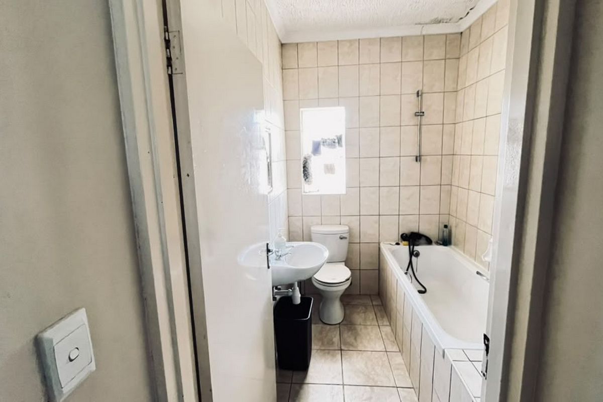 A compact bathroom featuring a bathtub, pedestal basin, and toilet with neutral wall and floor tiling, requiring some ceiling maintenance.