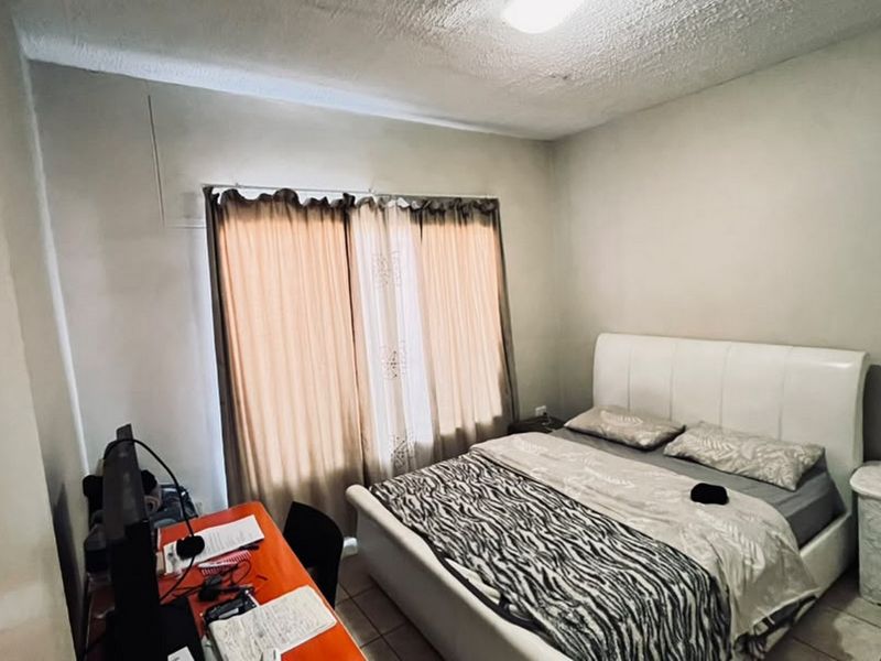 A bedroom featuring tiled flooring and a window with curtain tracks. The room requires cosmetic updates to the ceiling and wall finishes.