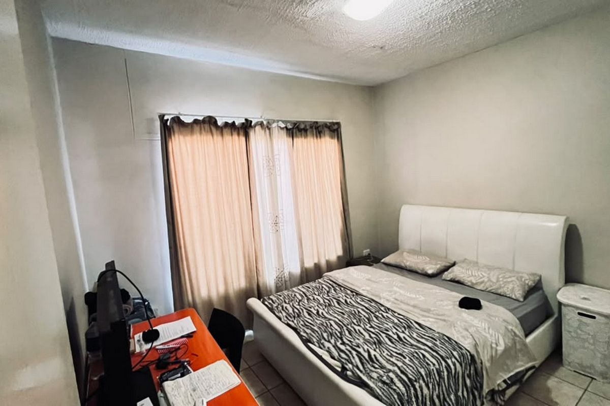 A bedroom featuring tiled flooring and a window with curtain tracks. The room requires cosmetic updates to the ceiling and wall finishes.