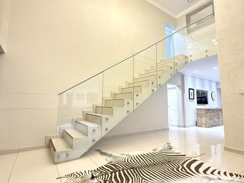 Grand entrance hall featuring a modern staircase with a frameless glass balustrade, polished floor tiles, and an elegant chandelier.