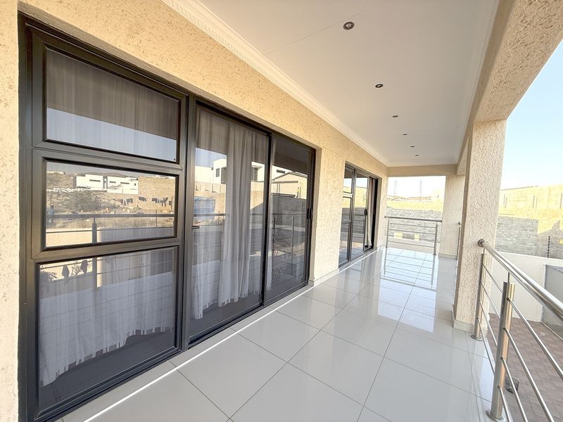 A spacious, modern covered balcony featuring sleek tiled flooring, stainless steel balustrades, and large sliding glass doors providing seamless indoor-outdoor flow.