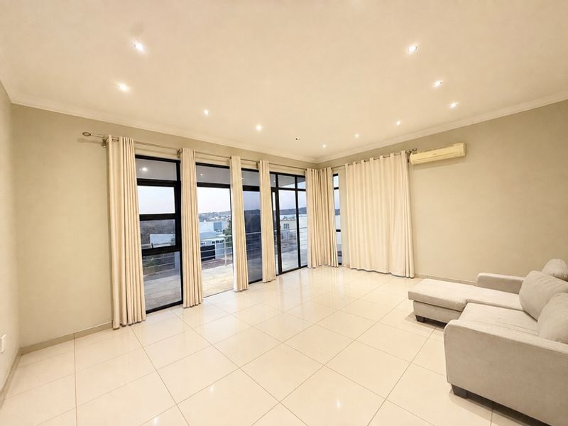 Spacious living area featuring large glass sliding doors, tiled flooring, recessed downlighting, and a wall-mounted split-system air conditioner.
