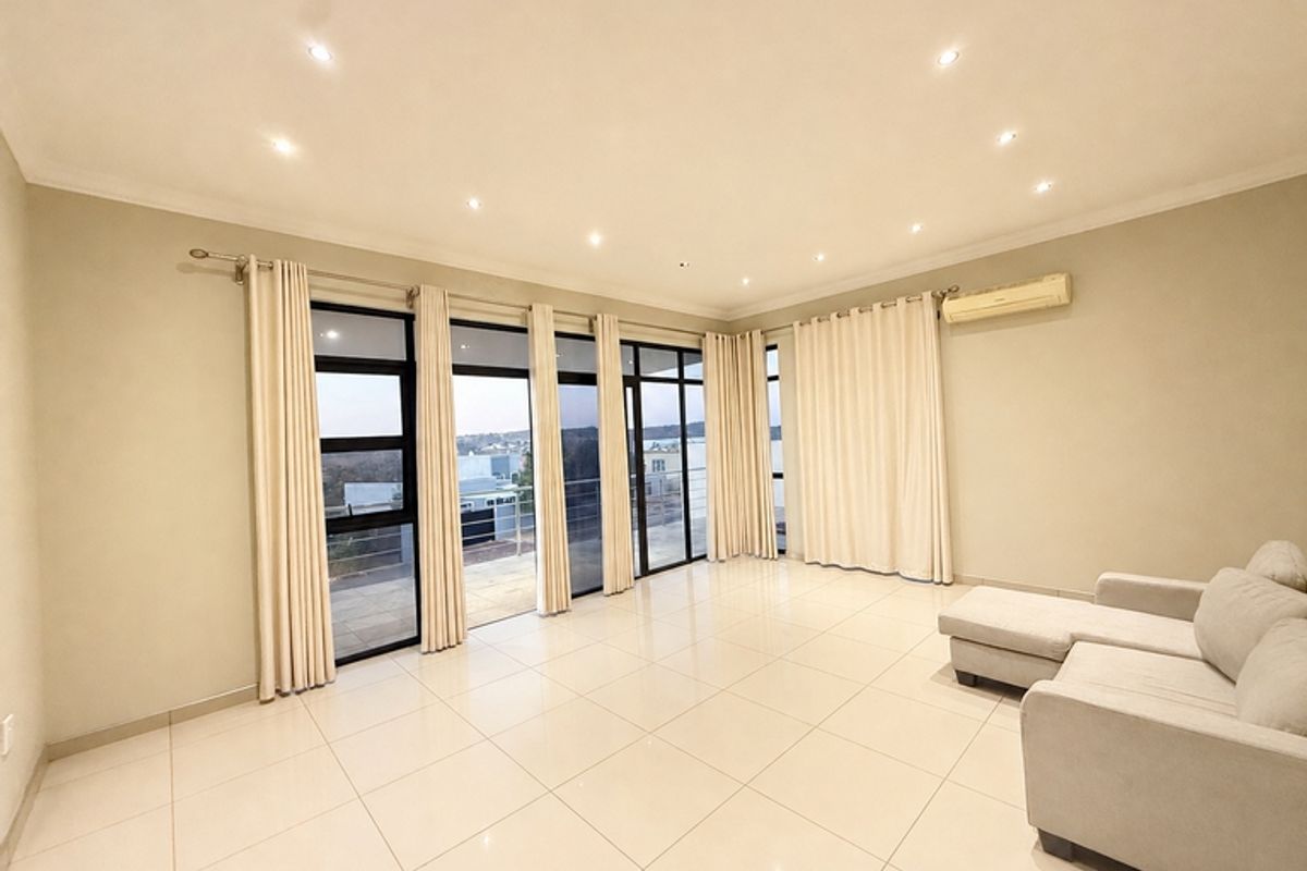 Spacious living area featuring large glass sliding doors, tiled flooring, recessed downlighting, and a wall-mounted split-system air conditioner.