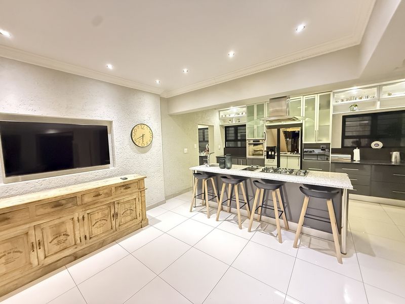 Modern open-plan living area featuring a sleek kitchen with a central island, gas hob, built-in oven, and a recessed wall niche for television mounting.