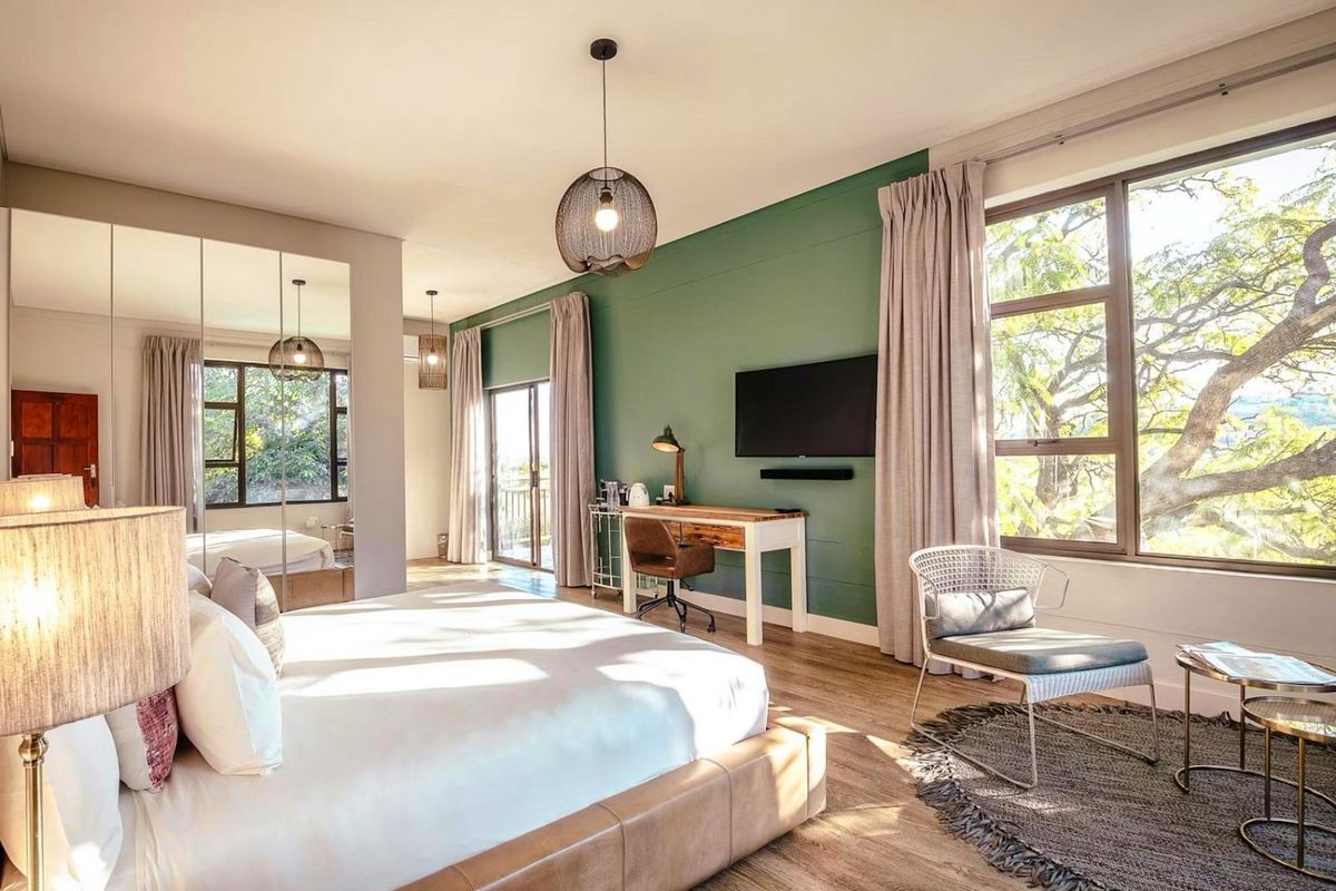 Spacious, well-lit bedroom featuring modern laminate flooring, large windows with natural views, and a built-in mirrored wardrobe.