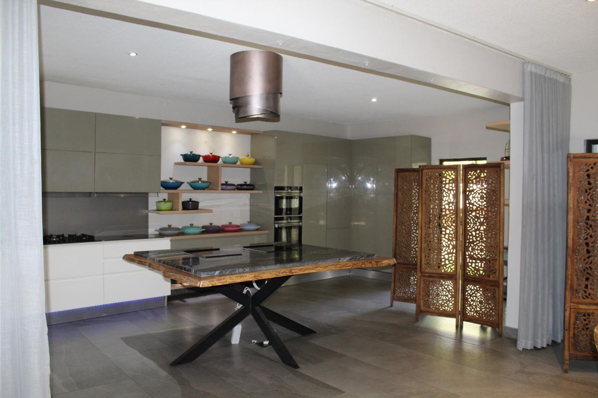 Modern kitchen featuring high-gloss cabinetry, integrated double ovens, a gas hob, and a striking stone-topped island with a unique base.
