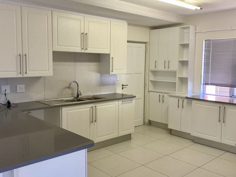 A clean, modern kitchen featuring white cabinetry, stone countertops, a double sink, and tiled flooring, offering a bright and functional workspace.