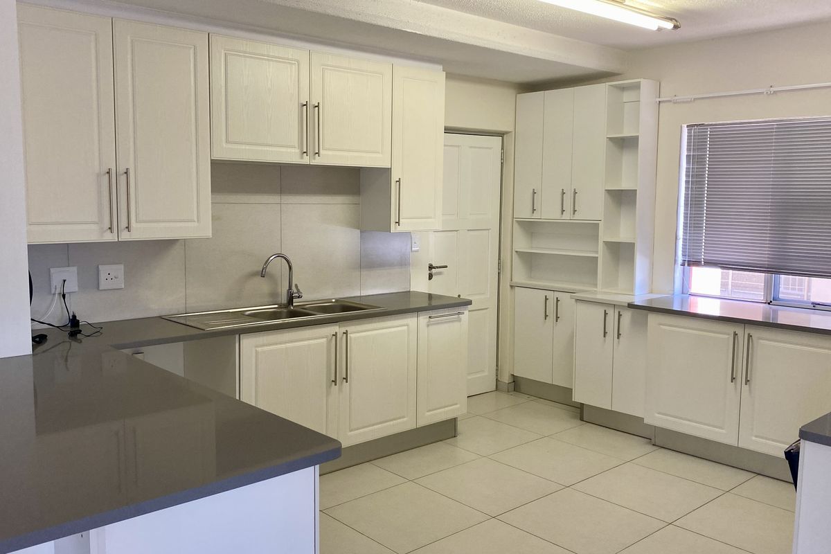 A clean, modern kitchen featuring white cabinetry, stone countertops, a double sink, and tiled flooring, offering a bright and functional workspace.