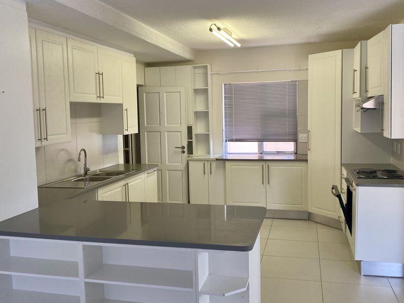 A clean, functional kitchen featuring white cabinetry, stone countertops, integrated appliances, and a breakfast bar, offering a bright and practical workspace.