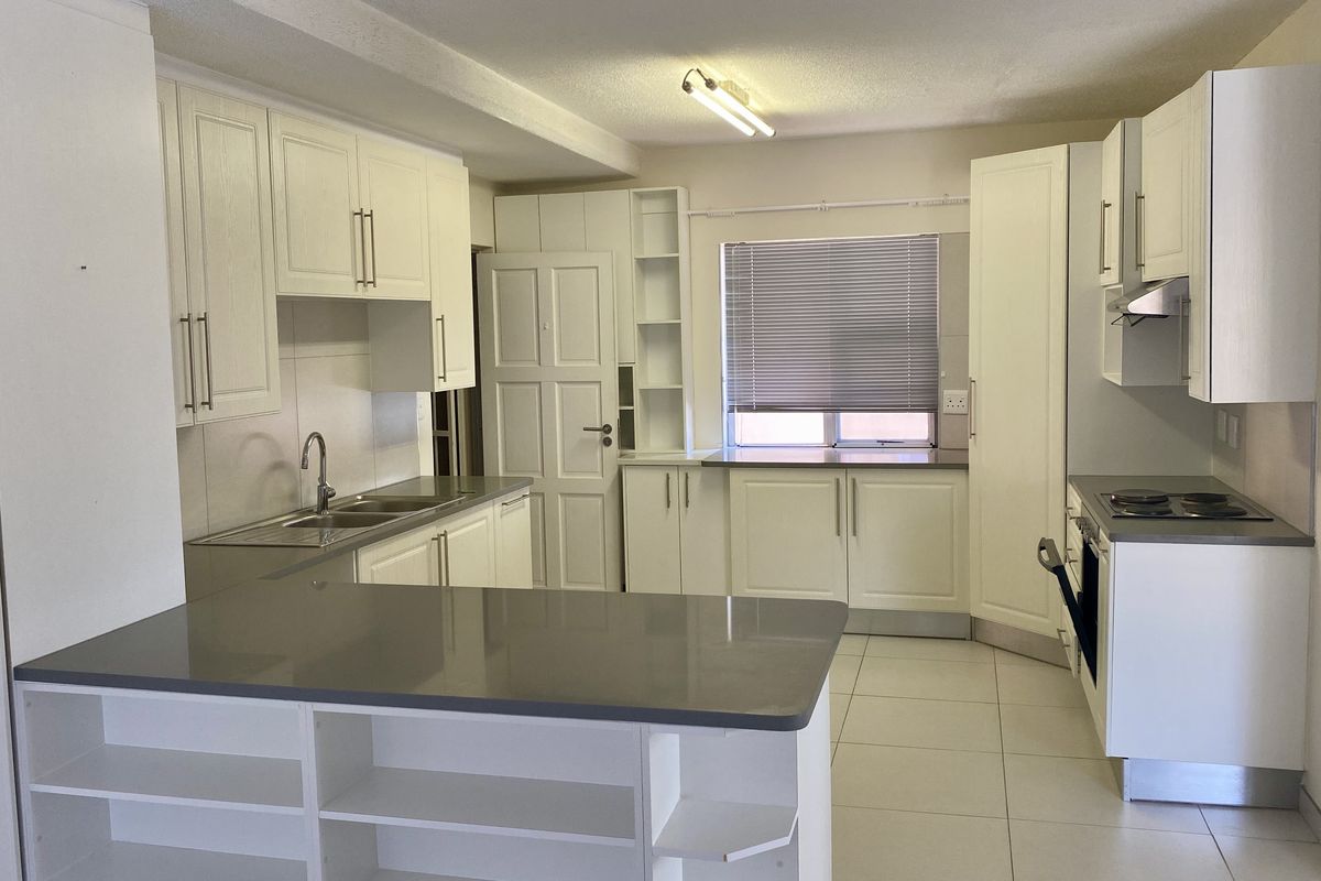 A clean, functional kitchen featuring white cabinetry, stone countertops, integrated appliances, and a breakfast bar, offering a bright and practical workspace.