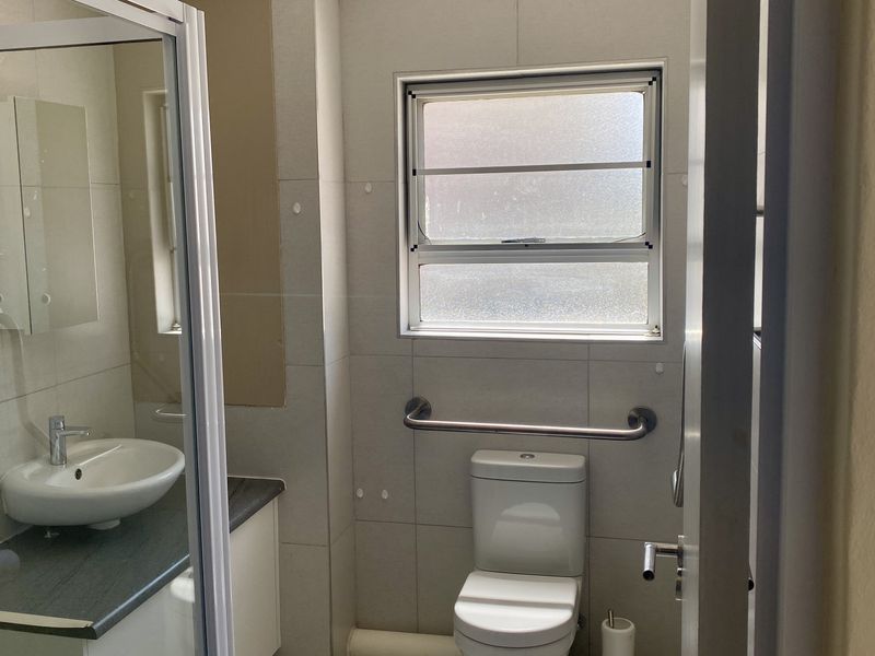 A functional bathroom featuring a vanity with basin, a toilet with a safety grab rail, and a glass-enclosed shower area with tiled walls.