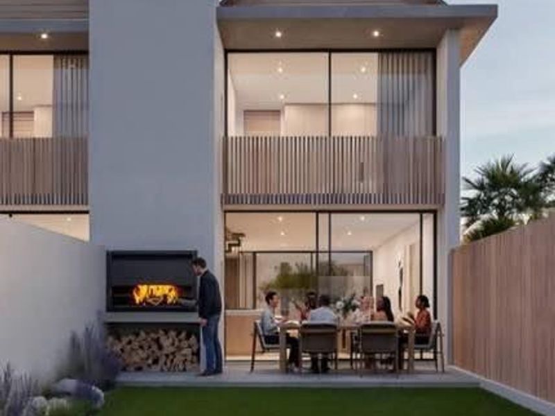 Modern townhouse rear elevation featuring a landscaped garden, concrete patio with built-in braai, and upper-level balcony with timber slat detailing.