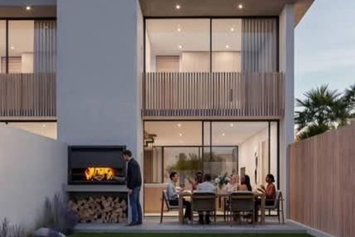 Modern townhouse rear elevation featuring a landscaped garden, concrete patio with built-in braai, and upper-level balcony with timber slat detailing.