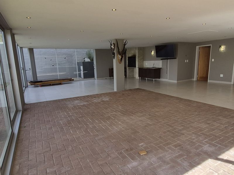 Spacious open-plan living area featuring a built-in braai, large sliding glass doors, and a combination of brick and tile flooring.