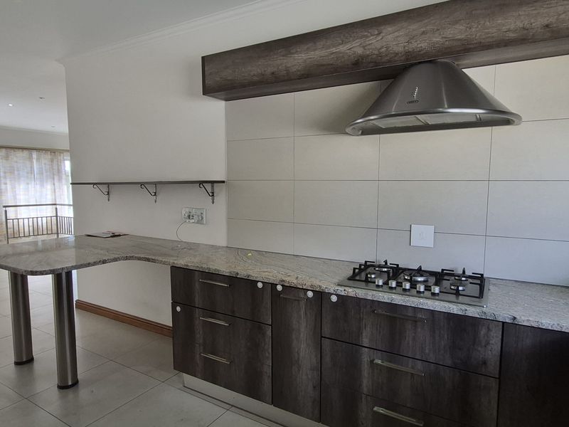Modern kitchen featuring granite countertops, a gas hob with stainless steel extractor fan, and ample built-in cabinetry, seamlessly flowing into the adjacent living area.