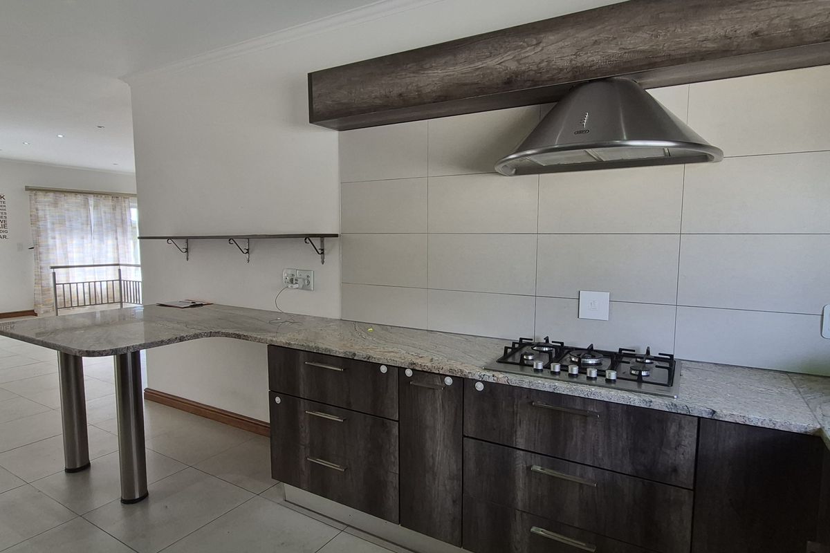 Modern kitchen featuring granite countertops, a gas hob with stainless steel extractor fan, and ample built-in cabinetry, seamlessly flowing into the adjacent living area.