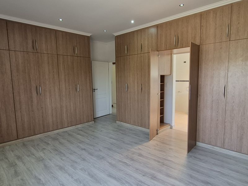 Spacious bedroom featuring extensive floor-to-ceiling built-in wooden cabinetry, modern laminate flooring, and recessed lighting, offering ample storage and a clean, neutral aesthetic.