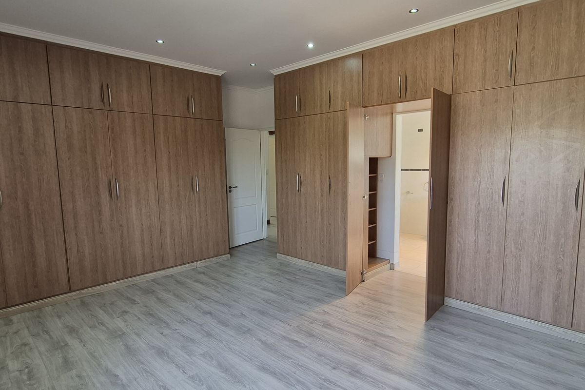 Spacious bedroom featuring extensive floor-to-ceiling built-in wooden cabinetry, modern laminate flooring, and recessed lighting, offering ample storage and a clean, neutral aesthetic.
