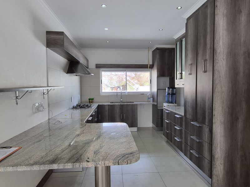 Modern kitchen featuring granite countertops, extensive built-in cabinetry, gas hob, extractor fan, and tiled flooring in a clean, well-lit space.