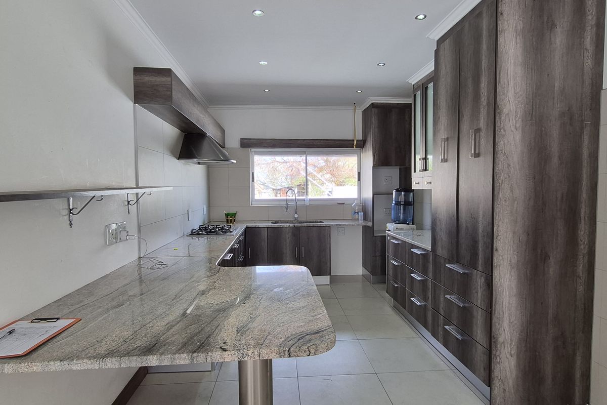Modern kitchen featuring granite countertops, extensive built-in cabinetry, gas hob, extractor fan, and tiled flooring in a clean, well-lit space.