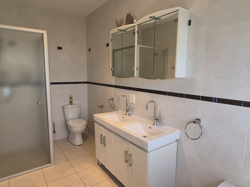 A functional bathroom featuring a double vanity with a mirrored cabinet, a glass-enclosed shower, and a toilet, finished with neutral wall and floor tiles.