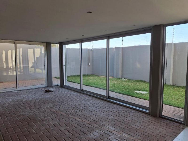 A spacious, covered patio area featuring large sliding glass doors that open onto a private garden, finished with durable paved flooring and recessed lighting.