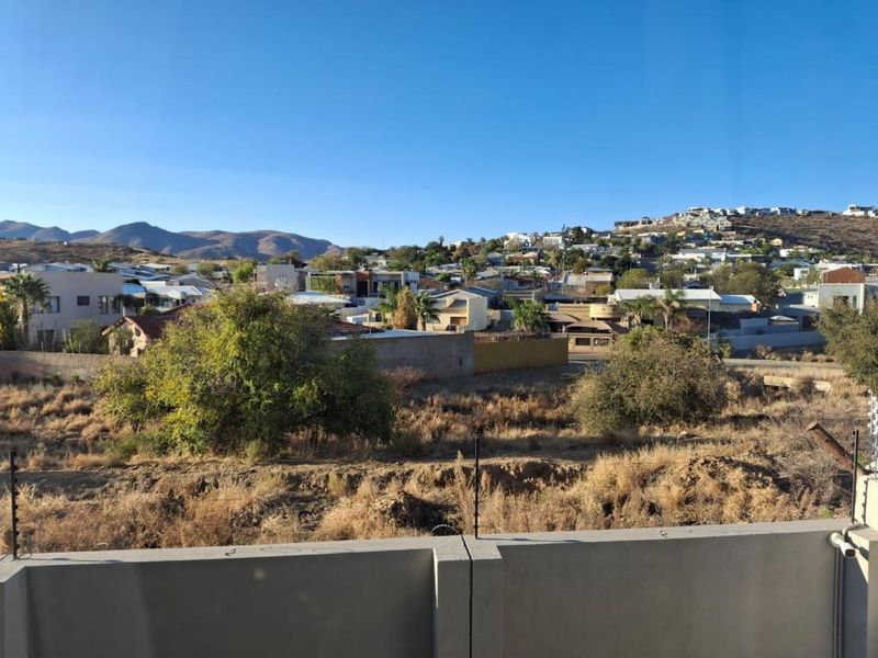 An elevated view overlooking the surrounding residential neighbourhood and distant hills, featuring a concrete perimeter wall with electric fencing in the foreground.