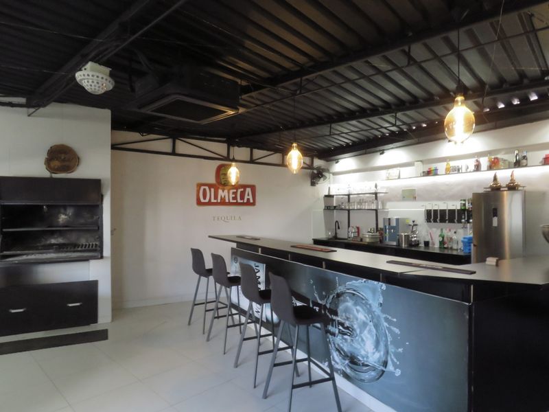 A dedicated entertainment bar area featuring a built-in bar counter, integrated braai, exposed ceiling, and modern pendant lighting.