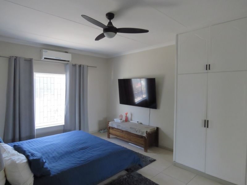 A well-maintained bedroom featuring tiled flooring, a built-in wardrobe, a ceiling fan, and a wall-mounted air conditioning unit.