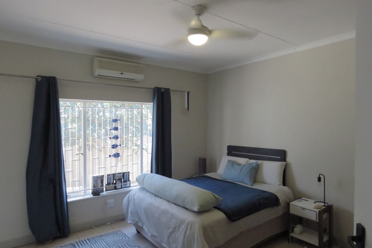 A functional bedroom featuring tiled flooring, a ceiling fan, and a wall-mounted split-system air conditioner for climate control.